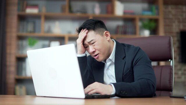 frustrated asian business man working at computer. Fail sitting at working desk with laptop in office. Irritated executive under stress problems disappointed with results while browsing pc. Asia 