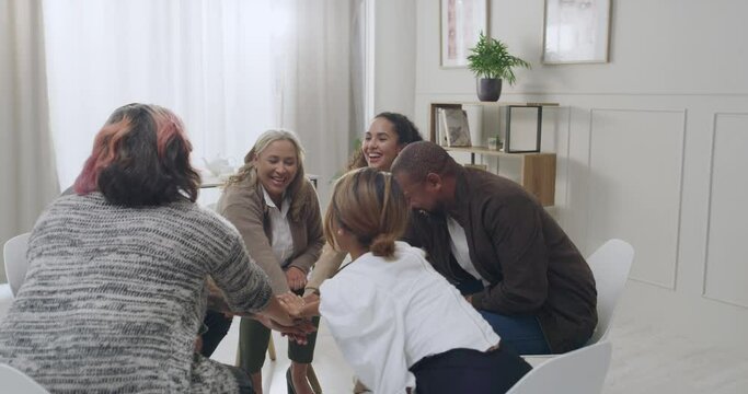 International employees showing unity and teamwork while feeling motivated during team building session.Diverse support group stacking and clapping hands during counselling with life coach, therapist.
