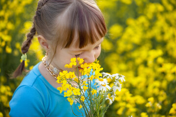 Smiling Little kid girl holding bouquet of fields yellow flowers and chamomiles enjoying summer day. Child giving flowers