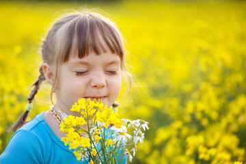 Smiling Little kid girl holding bouquet of fields yellow flowers and chamomiles enjoying summer day. Child giving flowers