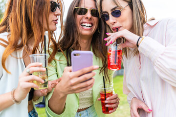 Group of smiling friends watching smart mobile phones - Teenagers addiction to new technology trends - Concept of youth, tech, social and friendship – happy young people having fun looking mobile phon