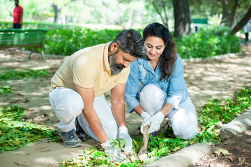 Happy indian couple planting tree in soil outdoor garden activity. environment and reforestation...
