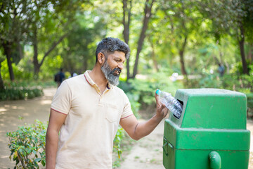 Happy Indian man throw empty litter in recycling bin, Asian male drop plastic bottle into garbage bin, pollution or waste management and save environment concept. - obrazy, fototapety, plakaty