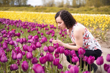 Obraz na płótnie Canvas Caucasian Adult Woman looking at fresh Tulip Flowers in a field. Spring Season.