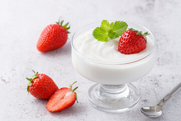 Milk pudding or yogurt with ripe strawberry berries and mint leaves  in glass bowl  closeup on stone background. Healthy vitamins and minerals food.