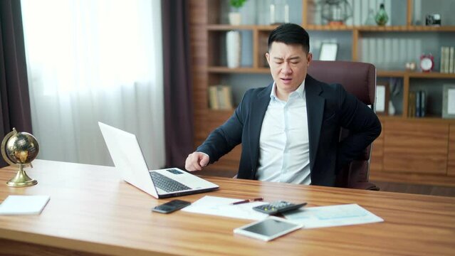 Tired worker businessman working in office sitting at computer desk long time, employee has severe back pain in workplace. Asian business man clerk syndrome sedentary work suffer from hurt, ache. Asia