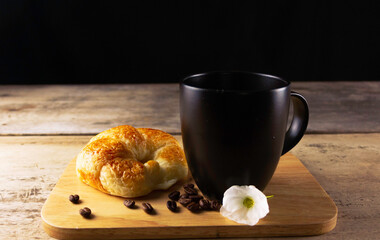 Cup of coffee with croissant ,pile of roasted coffee beans on an old rustic wooden table black background. Studio shot.