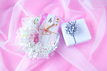 ウェディングイメージ　白い花の白いリースと結婚祝いの熨斗袋と贈り物（オーガンジー。ピンクバック）