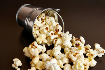 Small bucket filled with popcorn on a black background.