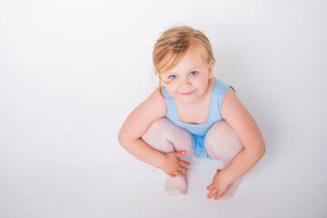cute little chubby girl in a blue dance leotard sitting on a white background looking up from the...