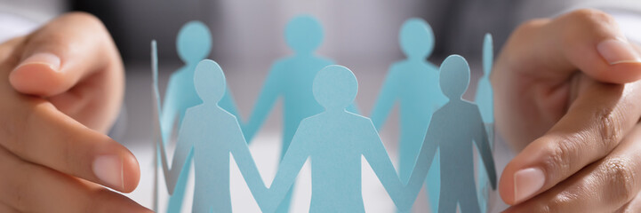 Businessperson Hand Protecting Paper Cut Out Figure On Table