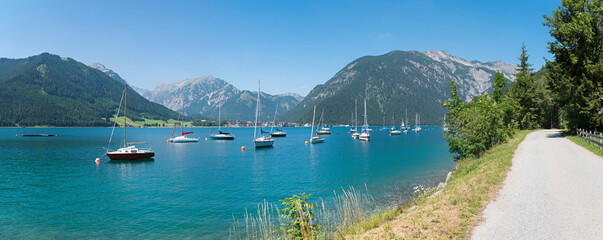 walkway along lake Achensee, many moored sailboats in the water. tirolean landscape - obrazy, fototapety, plakaty