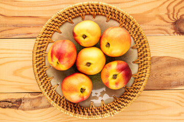 Several ripe juicy nectarines with a ceramic dish on a wooden table, close-up, top view.