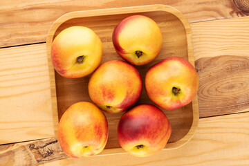 Several ripe juicy nectarines with a bamboo plate on a wooden table, close-up, top view.
