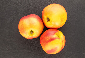Three ripe juicy nectarines on a slate stone, close-up, top view.