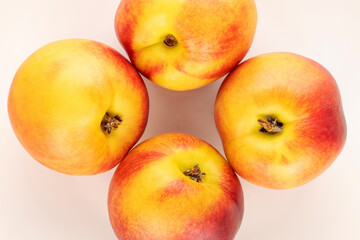 Four ripe juicy nectarines on a white ceramic plate, close-up, top view.