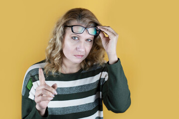 A woman with a stern look looks out from under her glasses and shows a sign of attention, a...