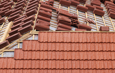 Obraz na płótnie Canvas Roofing construction with clay roof tiles. Roofer laying ceramic roof tiles. Lay roof tiles