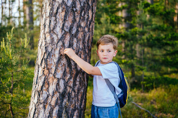 Portrait of ecologist or traveler boy with backpack hugging tree and looking aside.