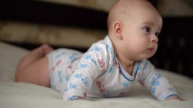 Newborn Active Baby Cute Smiling Teethless Face Portrait Early Days On Stomach Developing Neck Control. 5 Months Child On White Bed Looking on Camera. Infant, Childbirth, Parenthood, Beginning Concept