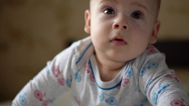 Newborn Active Baby Cute Smiling Teethless Face Portrait Early Days On Stomach Developing Neck Control. 5 Months Child On White Bed Looking on Camera. Infant, Childbirth, Parenthood, Beginning Concept