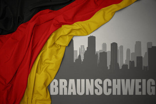 abstract silhouette of the city with text Braunschweig near waving national flag of germany on a gray background.