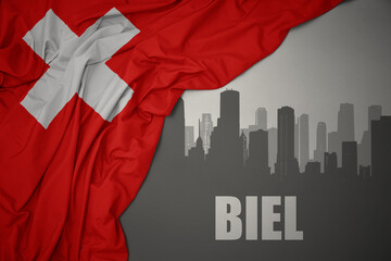 abstract silhouette of the city with text Biel near waving national flag of switzerland on a gray background. - obrazy, fototapety, plakaty