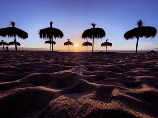 Straw sun umbrella silhouettes under blue sky sunset in Reñaca beach, Chile. Footprints on sand at splendid dusk. Summer tourism destination in Valparaiso Region