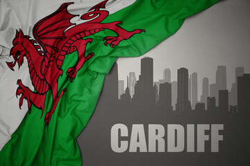 abstract silhouette of the city with text Cardiff near waving national flag of wales on a gray background.