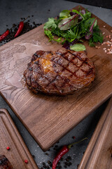 Fresh juicy delicious beef steak on a dark background. Meat dish with spices and herbs