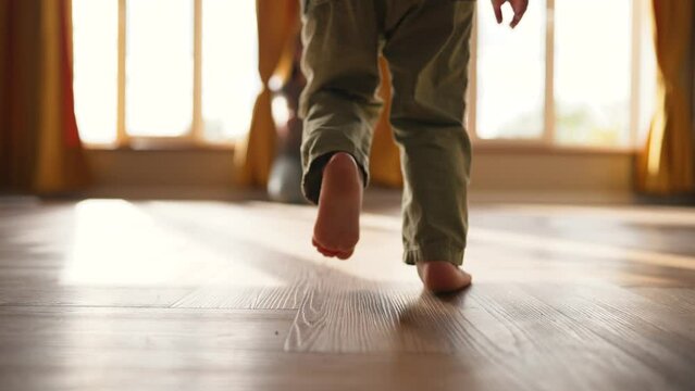 Baby takes first step on floor to his mother with bare feet.Son and mother at home feet on floor.Happy boy barefoot on laminate.Baby foot on wooden floor.Child is learning to walk.Happy family concept
