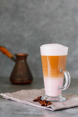 Latte macchiato and roasted coffee beans on a linen napkin. Latte macchiato coffee with rose milk on a gray background. Copy space
