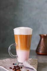 Latte macchiato and roasted coffee beans on a linen napkin. Latte macchiato coffee with rose milk on a gray background. Copy space
