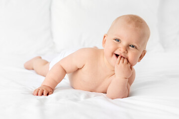 Smiling baby girl lying on bed with fingers in mouth