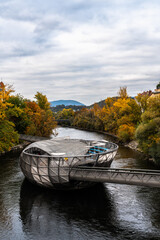 Beautiful view of Murinsel island on the Mur river with colorful trees and mountains in background on a cloudy autumn day, Graz, Austria - 513198685