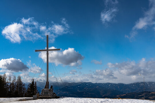 Panorama aerial view of Alps in south of Styria from top of Schöckl near Graz with the summit cross and  blue sky cloud on sunny winter day, Sankt Radegund, Austria