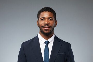 Front view portrait of adult black man wearing business suit and smiling at camera against plain...