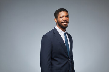 Portrait of adult black man wearing business suit and smiling at camera while standing against grey background in studio, copy space