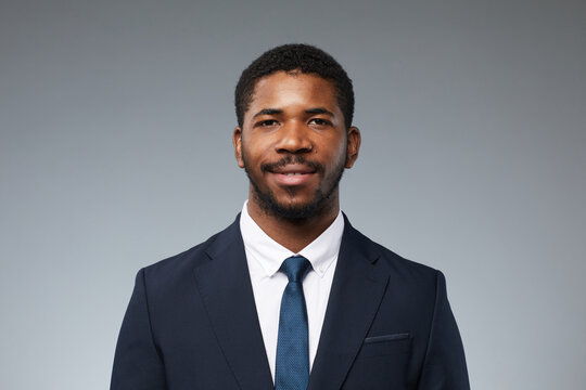 Front view portrait of adult black man wearing business suit and smiling at camera against plain grey background
