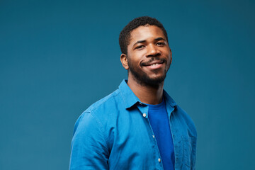 Obraz premium Portrait of smiling African American man wearing blue on blue background and looking at camera, copy space