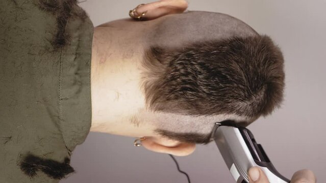 A woman is shaved with an electric razor with her back to the camera, leaving a large mohawk. vertical video