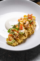 delicious Creamy Parmesan Linguine with Shrimps sprinkled with finely chopped parsley in skillet on black wooden table with piece of cheese and uncooked pasta, horizontal view from above