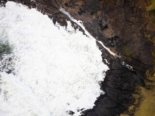 Fototapeta premium Shooting from the air. Foaming ocean, storm. Rocky uneven coast. Desert place, wild nature. Element, danger. Ecology, geology, cartography. The beauty and majesty of nature.