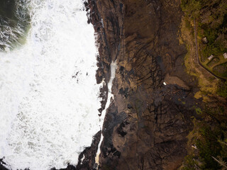 Top view of the ocean shore against which white foamy waves beat. Green grass on the shore. Storm, elements, beauty of nature. There are no people in the photo. Ecology, geology.