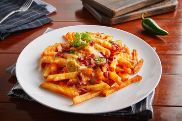Crispy cheesy fries served in a dish isolated on wooden background side view