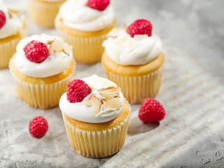 Lots of whipped cream muffins garnished with raspberries and almonds on a white background. Light sweet dessert. Restaurant, hotel, cafe, confectionery, supermarket.