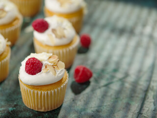 Appetizing muffins with cream and raspberries on a dark green background. There are no people in the photo. There is a space for insertion. Banner, birthday invitation.