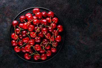 Ripe cherry on a black plate. Sweet cherries on a dark background. Healthy summer food concept. Copy space