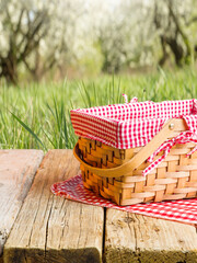 Against the background of a picturesque summer nature, a wooden table and a picnic basket on a pink checkered napkin. Picnic, outdoor recreation, vacation, day off, romance. - 513203887