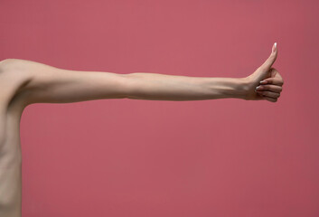 Young woman's stretched skinny arm thumb up. Isolated on pink background